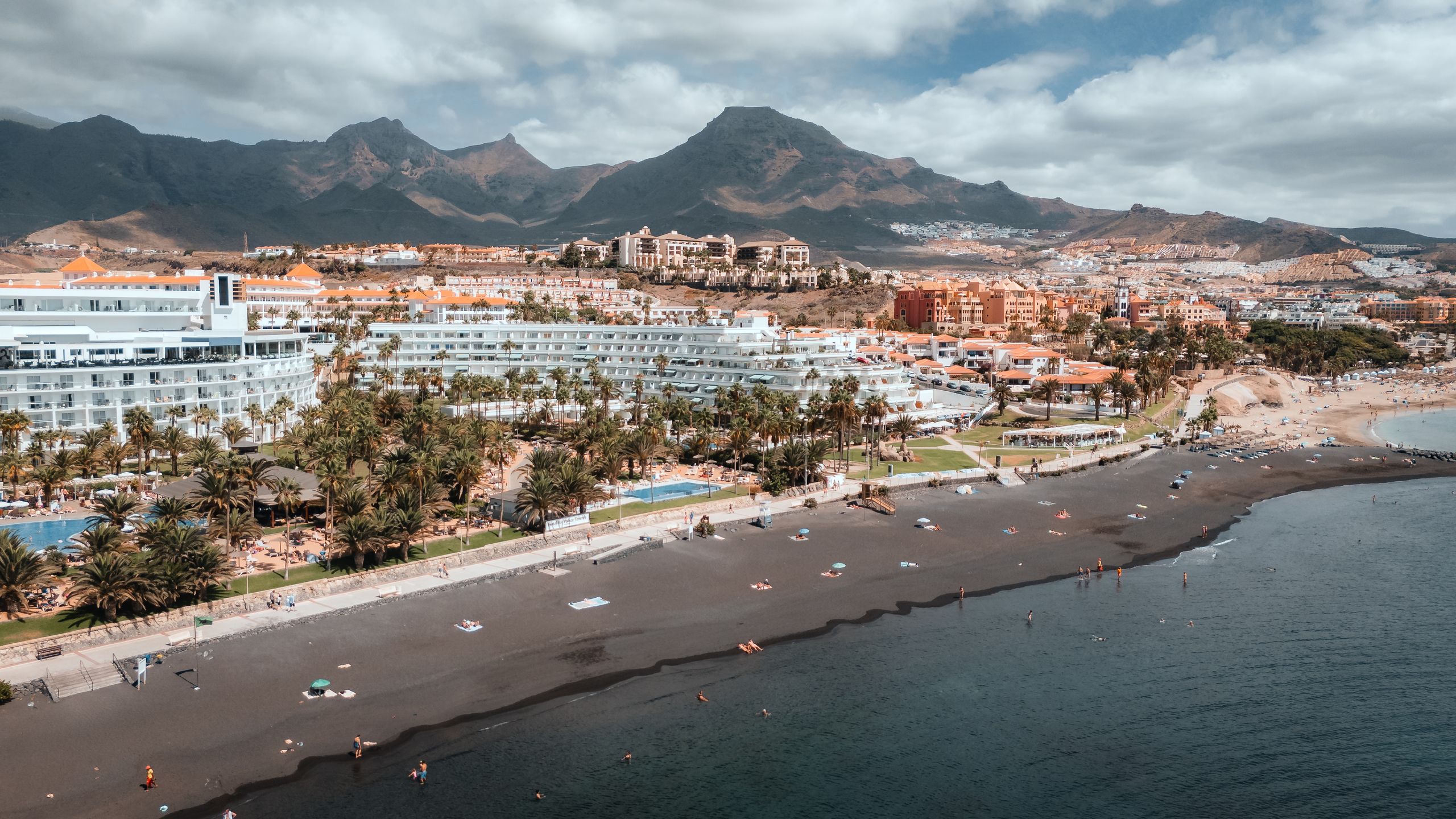 Scenic aerial shot of Adeje's beachside resorts with majestic mountains as a backdrop on a sunny day.